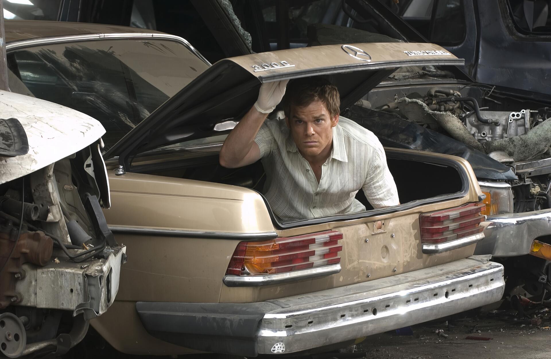Man emerging from a car trunk in a junkyard; 2K Quad HD PC desktop wallpaper. Tagged: TV show, Dexter. I don't know the person's identity.