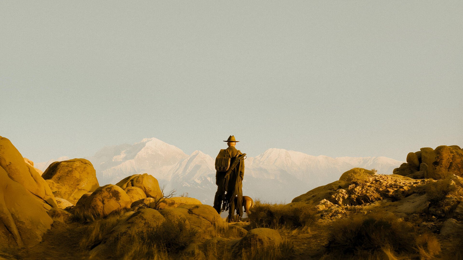 Fallout TV show 4K Ultra HD PC wallpaper: a lone cowboy and dog stand on a rocky outcrop overlooking distant snowy peaks under a vast yellow-tinted sky.