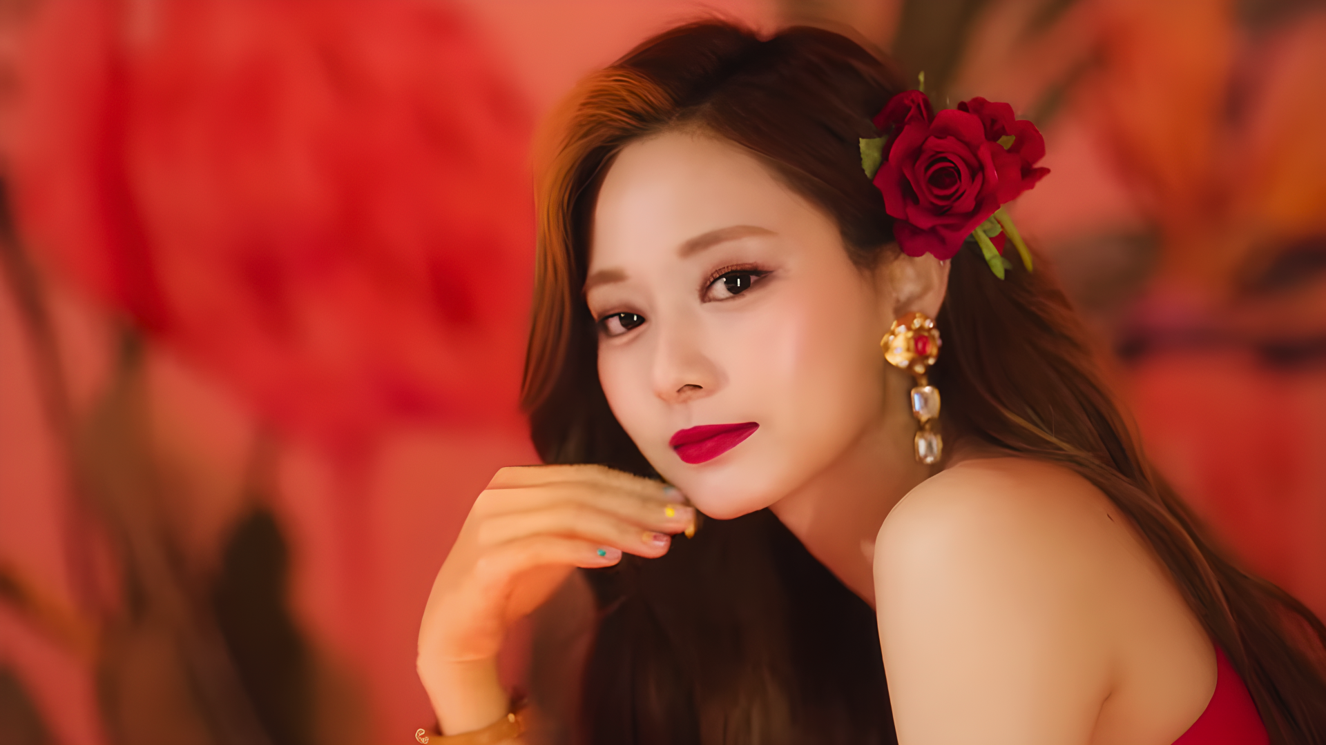 HD desktop wallpaper of a k-pop idol with summer vibes — red rose tucked behind her ear, glamorous earrings and a warm, blurred floral backdrop.