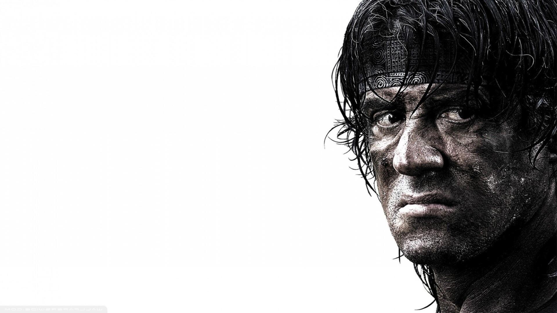 Close-up of a gritty, dirt-streaked Rambo from Rambo 4, intense stare and headband on a white background — HD PC desktop wallpaper.