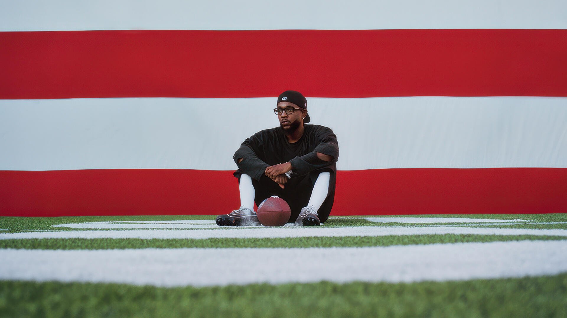 Rapper seated on turf holding a football against a bold red-and-white Super Bowl backdrop — 4K Ultra HD PC desktop wallpaper
