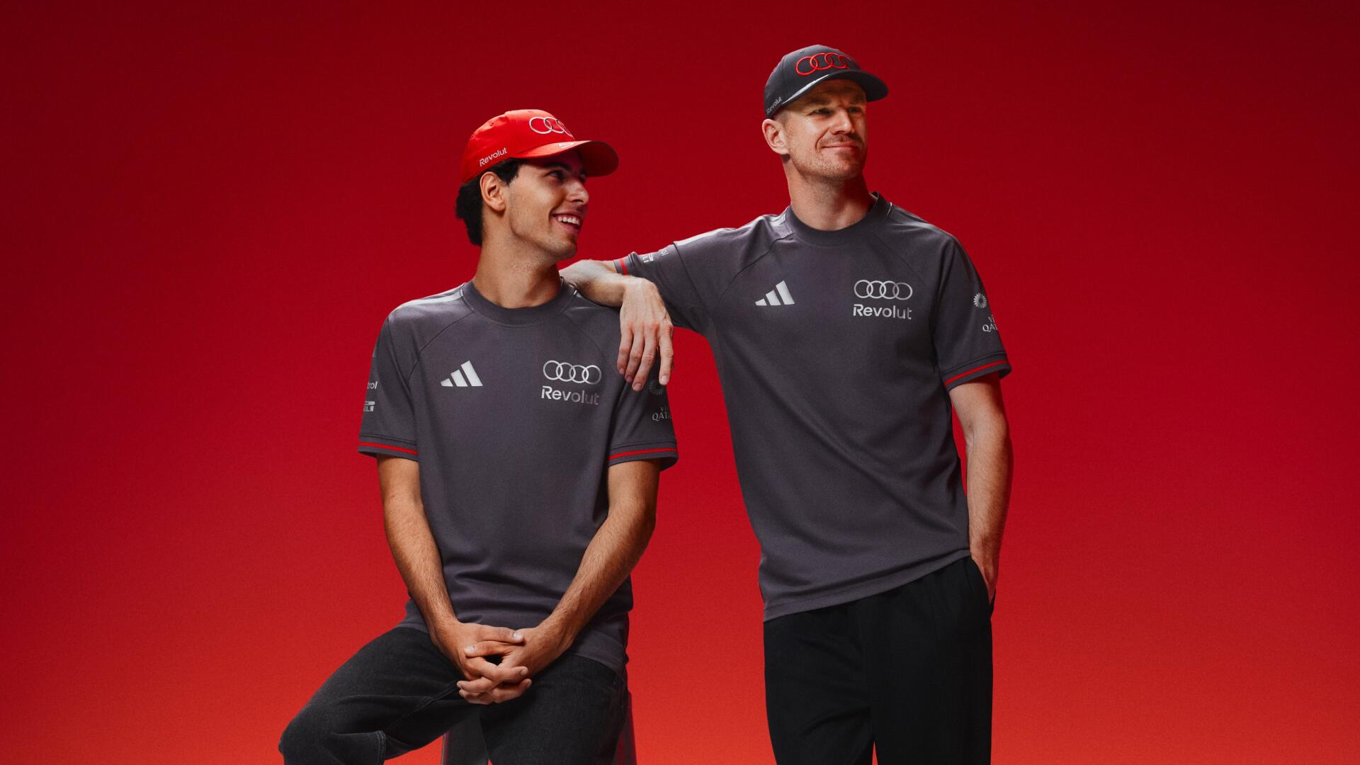 Two Audi F1 drivers in gray team shirts and red caps pose against a vivid red background — 4K Ultra HD PC desktop wallpaper.