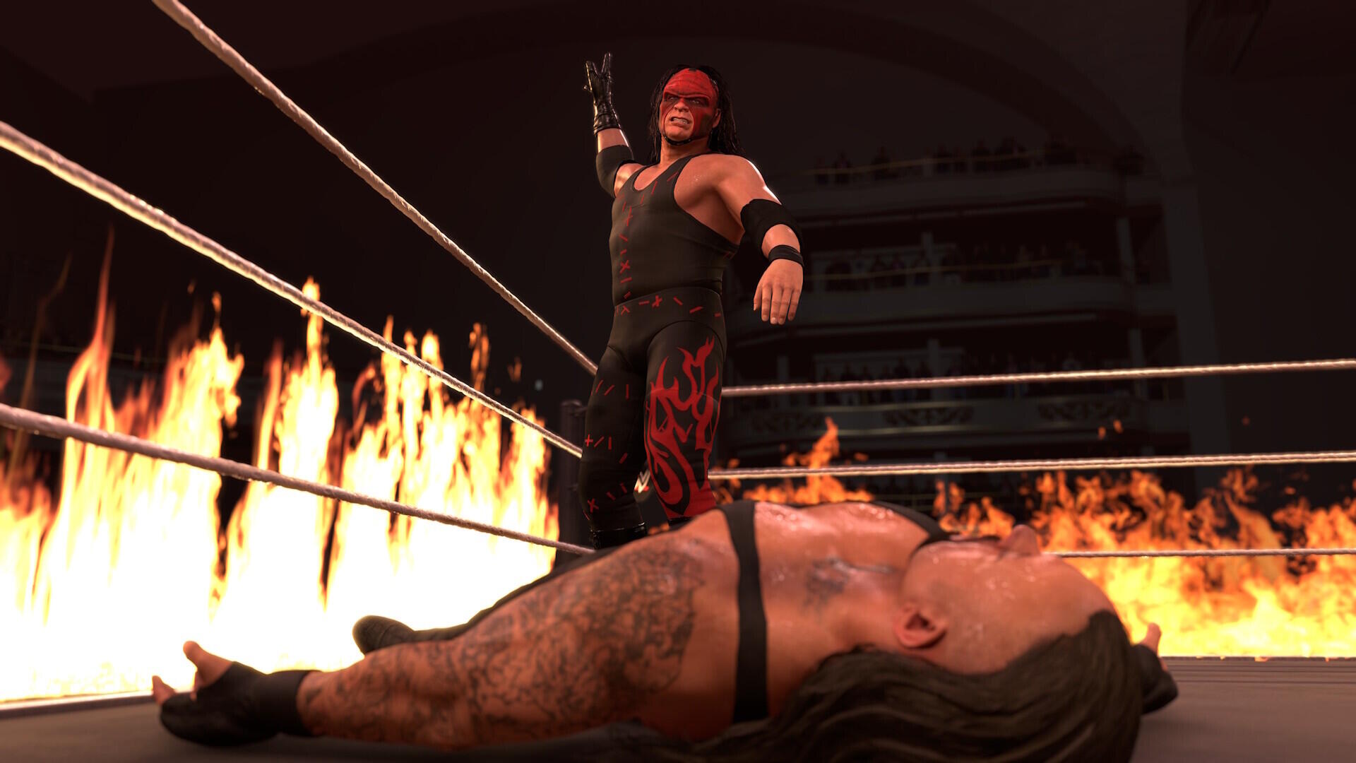 HD PC desktop wallpaper and background from the video game WWE 2K26: masked wrestler stands in a ring of flames over a fallen opponent.