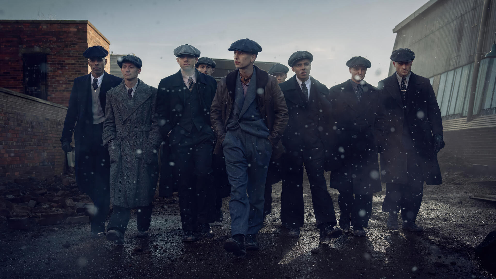 Peaky Blinders: The Immortal Man movie wallpaper — gang of flat-capped gangsters in overcoats stride through a rain-slick alley at dusk. 4K Ultra HD PC desktop background.