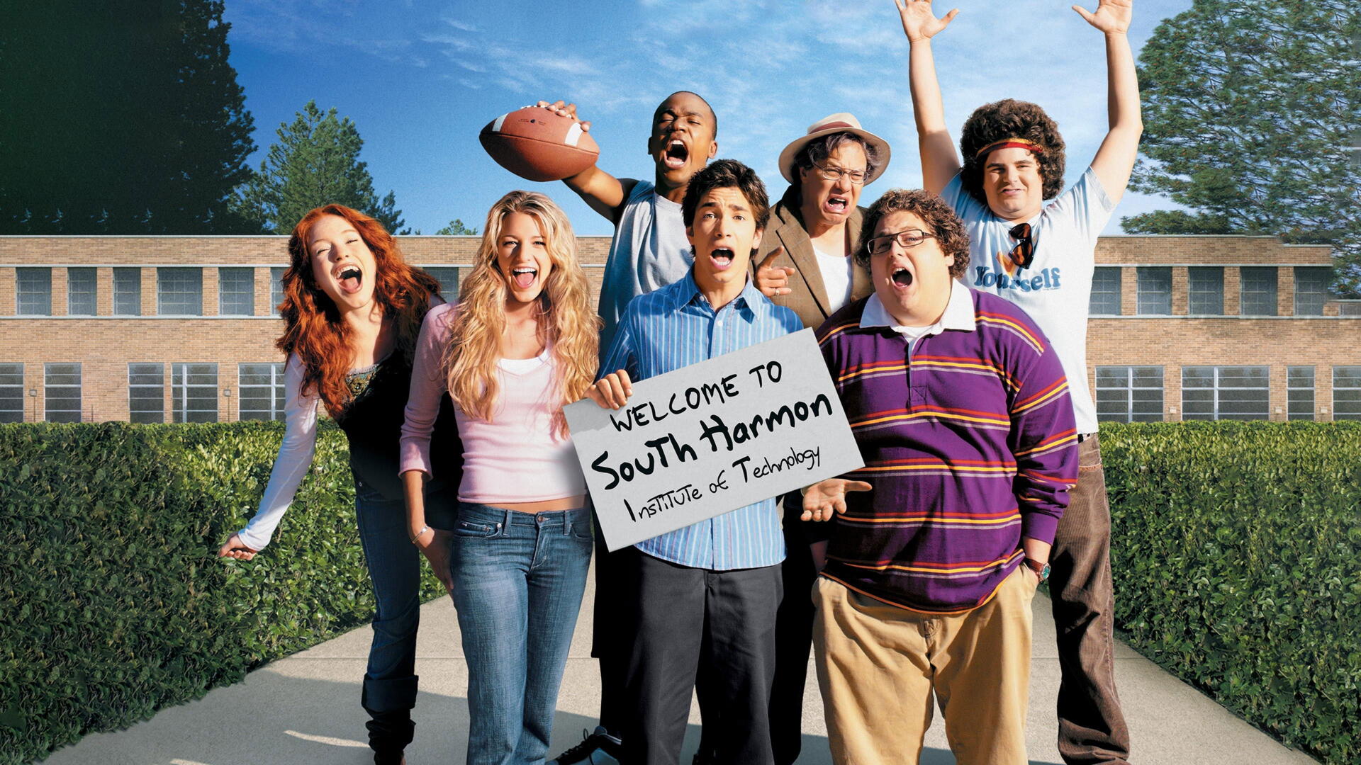 Accepted 4K Ultra HD PC desktop wallpaper: seven young adults pose outside a school, one holding a sign reading Welcome to South Harmon Institute of Technology beneath a clear blue sky.