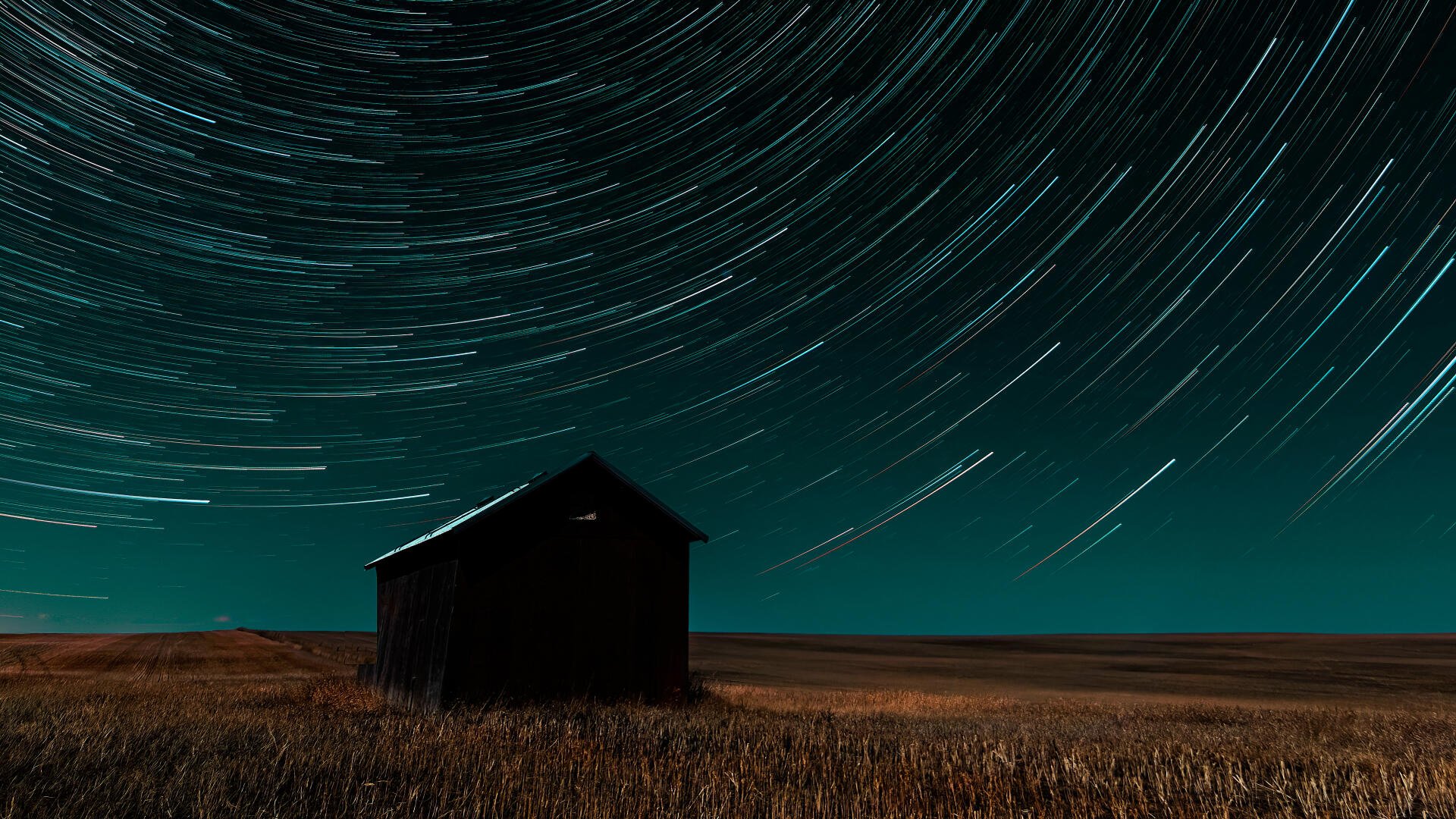 4K Ultra HD PC desktop wallpaper — nature time-lapse photography of star trails circling above a lone barn in a night field.