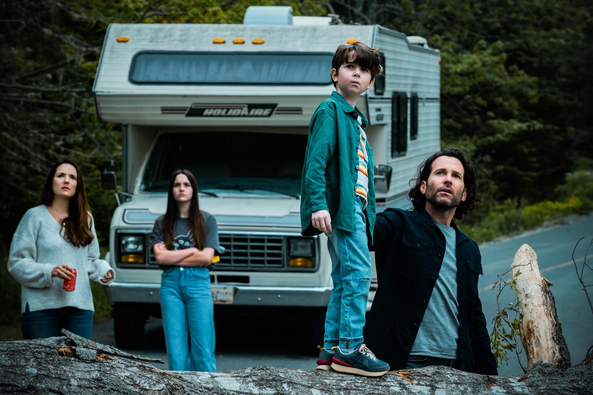 TV show From (2022) 5K Ultra HD PC desktop wallpaper: tense family of four — two adults and two youths — stand before a parked RV on a forest road under an overcast sky, wary expressions.