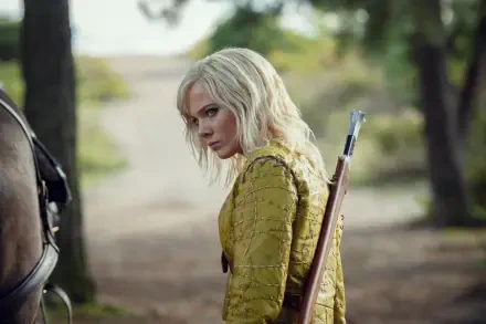 5K Ultra HD wallpaper: Ciri from The Witcher in a yellow coat with a bow slung on her back, glancing over her shoulder on a sunlit forest path.