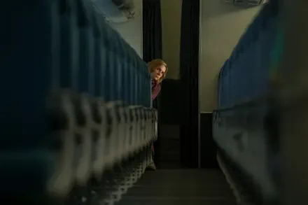 5K UHD desktop wallpaper from TV show Pluribus — a woman peeks between dim blue seats, framed by a narrow aisle.