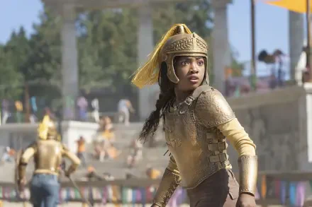 HD PC desktop wallpaper from the TV show Percy Jackson and the Olympians: a young warrior in gold armor and helmet stands alert in a sunlit stadium crowd.