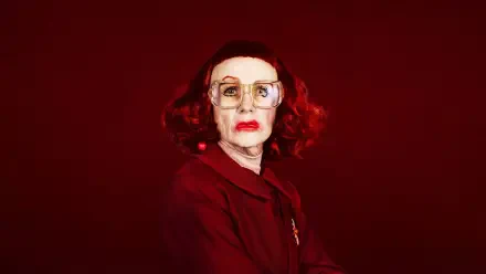 4K Ultra HD PC desktop wallpaper: portrait of an elderly woman with red hair and glasses against a deep red backdrop, weapon-themed, tense cinematic mood.