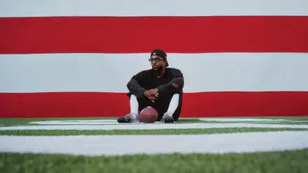 Rapper seated on turf holding a football against a bold red-and-white Super Bowl backdrop — 4K Ultra HD PC desktop wallpaper