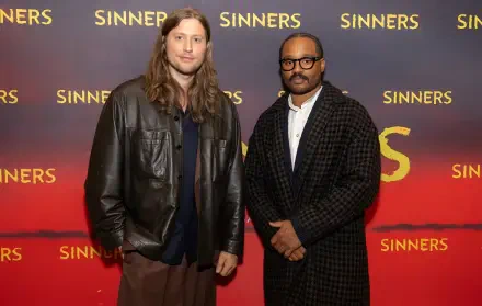 Two men in a leather jacket and a checkered coat pose before a red Sinners backdrop — 4K Ultra HD PC desktop wallpaper featuring two filmmakers.