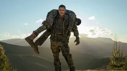 War Machine (2026) 4K Ultra HD PC desktop wallpaper: armored soldier carries a wounded comrade across a sunlit mountain ridgeline at dusk.