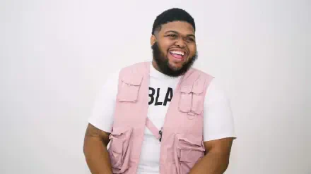 Laughing man in a pink utility vest over a white tee against a plain white backdrop, 2K Quad HD PC desktop wallpaper.