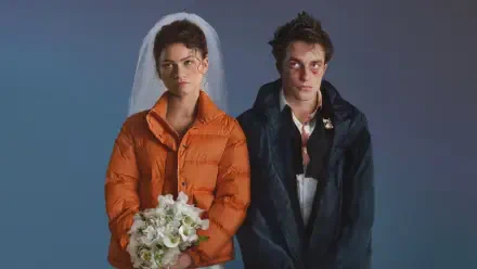 The Drama — 4K Ultra HD PC desktop wallpaper: a bride in an orange puffer jacket holding a bouquet stands beside a disheveled groom in a dark coat on a blue backdrop.