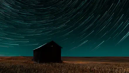 4K Ultra HD PC desktop wallpaper — nature time-lapse photography of star trails circling above a lone barn in a night field.
