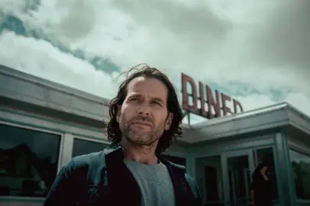 Long-haired man standing before a retro diner under stormy skies — TV show scene from 2022, presented as an 8K Ultra HD PC desktop wallpaper and background.