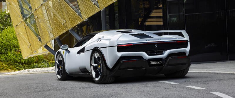 {{ White Ferrari SC40 vehicle shown rear three-quarter, parked by modern architecture - 2K Quad HD PC desktop wallpaper/background.