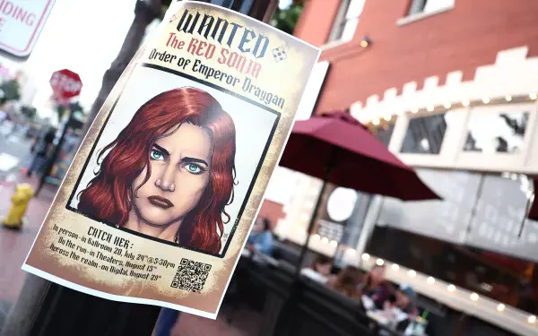 4K Ultra HD movie-style wanted poster of Red Sonja on a street pole — illustrated red-haired warrior with blue eyes, 'WANTED' headline; PC desktop wallpaper background.