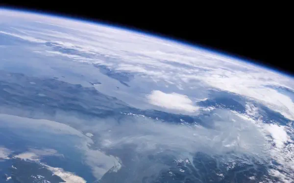 HD desktop wallpaper: expansive planetary landscape from orbit with curving horizon, cloud-covered surface and faint aurora borealis against the blackness of space.