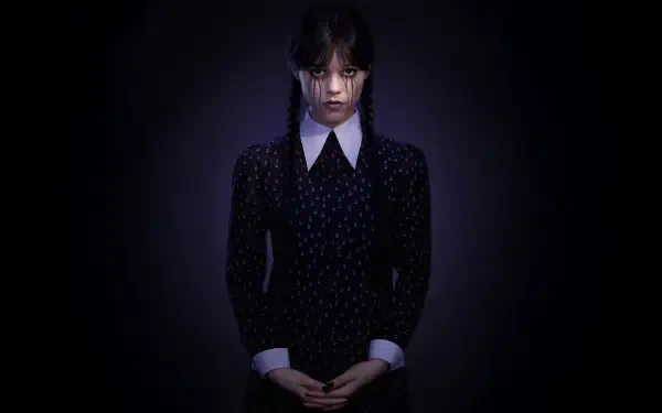 5K Ultra HD PC desktop wallpaper: Wednesday Addams in a dark dress with braided hair, pale face and clasped hands, spotlighted against a shadowy black background.