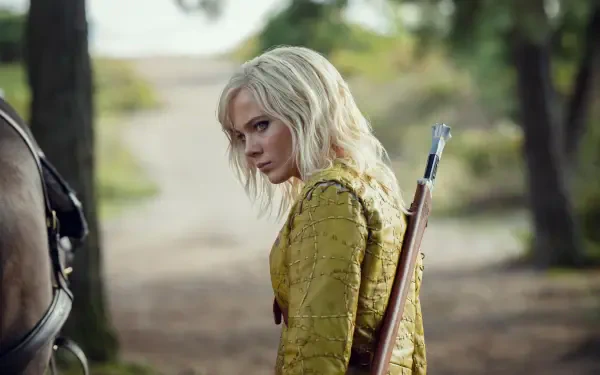 5K Ultra HD wallpaper: Ciri from The Witcher in a yellow coat with a bow slung on her back, glancing over her shoulder on a sunlit forest path.