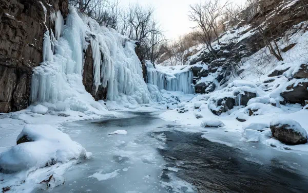 4K Ultra HD PC desktop wallpaper/background showing a nature scene: a frozen waterfall cascading into an icy river amid snow-covered rocks and leafless trees.