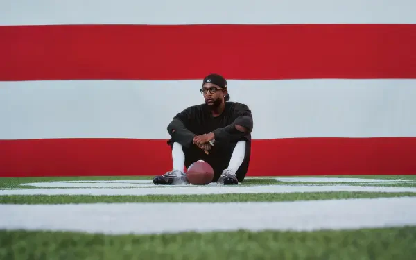Rapper seated on turf holding a football against a bold red-and-white Super Bowl backdrop — 4K Ultra HD PC desktop wallpaper