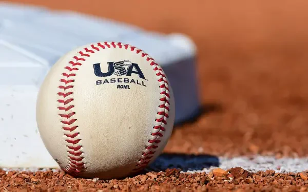 Close-up of a USA Baseball ball resting on infield dirt beside a base — sports-themed HD PC desktop wallpaper and background.