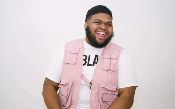 Laughing man in a pink utility vest over a white tee against a plain white backdrop, 2K Quad HD PC desktop wallpaper.