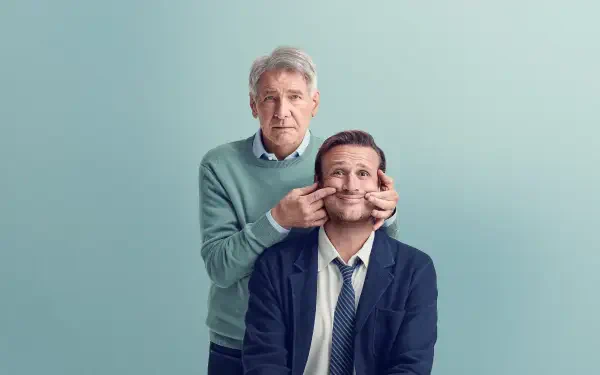 Shrinking-themed 4K Ultra HD PC desktop wallpaper: an older man playfully pinching the cheeks of a seated younger man against a soft teal background.
