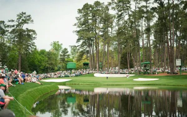 2K Quad HD PC desktop wallpaper — sports golf at The Masters: panoramic course view with green, water hazard, bunkers and spectators beneath tall pines.