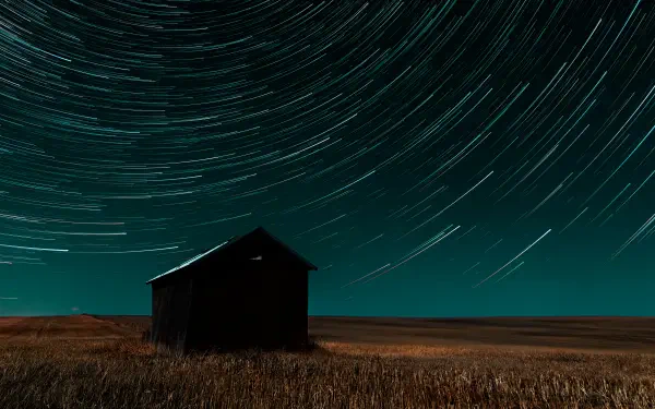 4K Ultra HD PC desktop wallpaper — nature time-lapse photography of star trails circling above a lone barn in a night field.