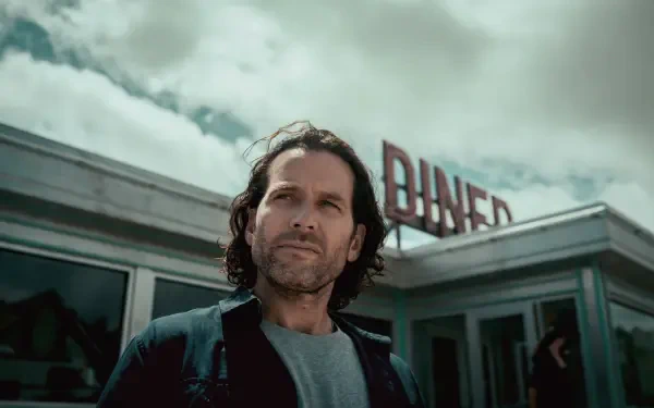 Long-haired man standing before a retro diner under stormy skies — TV show scene from 2022, presented as an 8K Ultra HD PC desktop wallpaper and background.