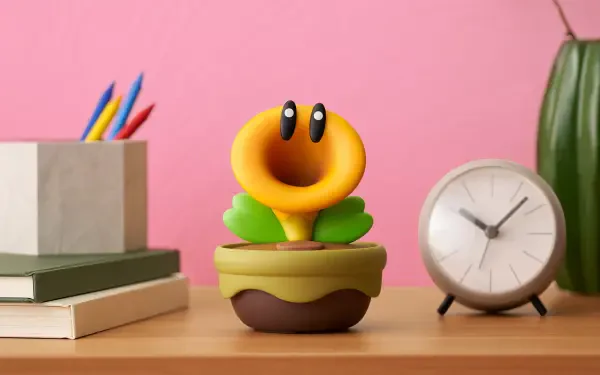 HD PC desktop wallpaper showing a Super Mario Bros. Wonder smiling yellow flower in a pot on a desk with books, pencils, an analog clock, and a pink wall background.