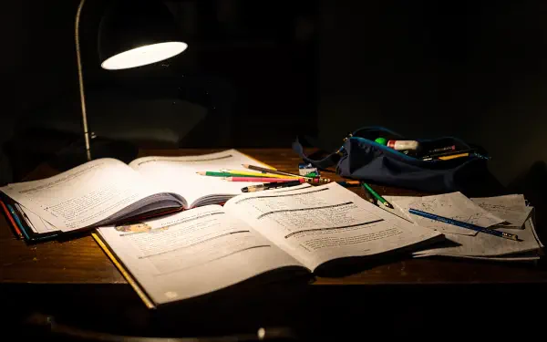 Homework scene: illuminated wooden desk with open notebooks, scattered pencils and a pencil case under a desk lamp — 4K Ultra HD PC desktop wallpaper and background.