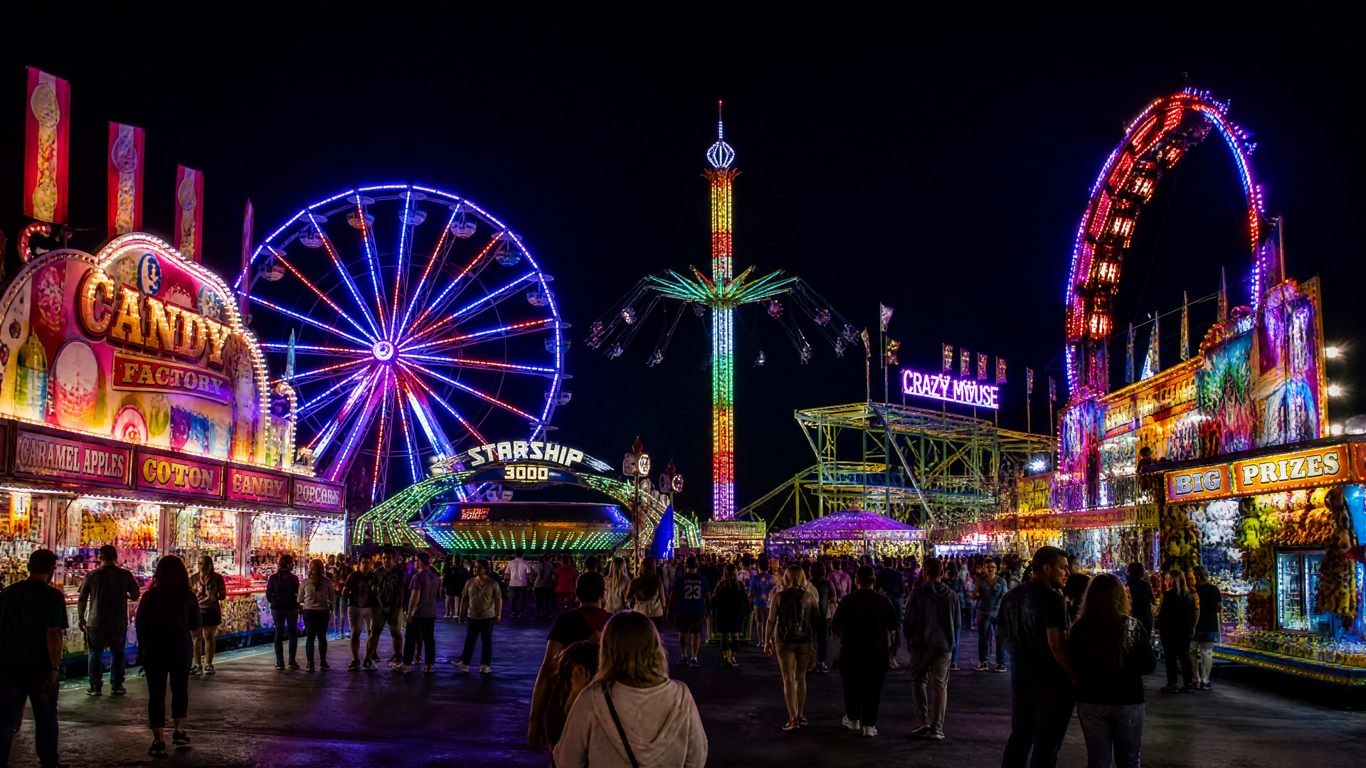 Vibrant nighttime fair scene with neon Ferris wheel, swing tower, arcade booths and strolling crowds — 4K Ultra HD PC desktop wallpaper and background.