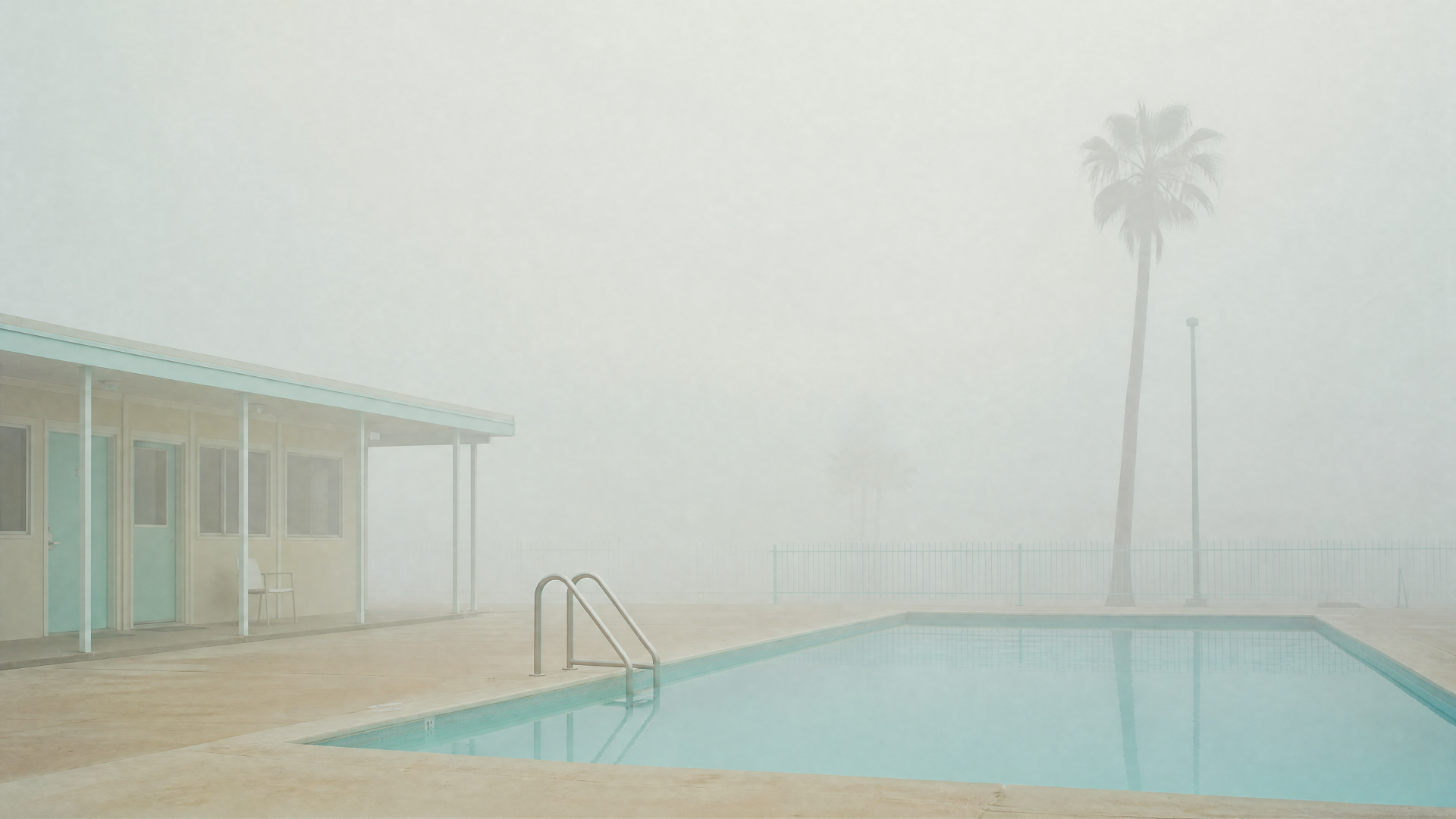 4K Ultra HD PC desktop wallpaper — foggy outdoor pool with ladder, pastel low building and lone palm tree, muted tones and minimalist, tranquil mood.