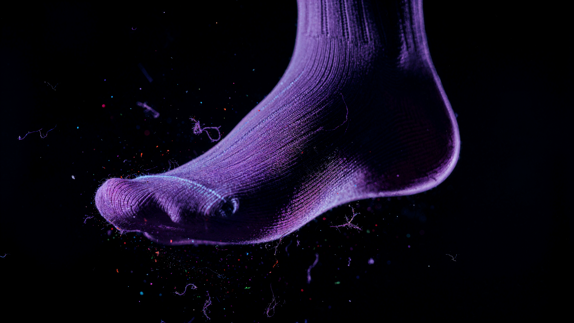 Close-up of a purple socked foot floating against a black backdrop, illuminated textile fibers and lint; 4K Ultra HD PC Desktop Wallpaper and Background.