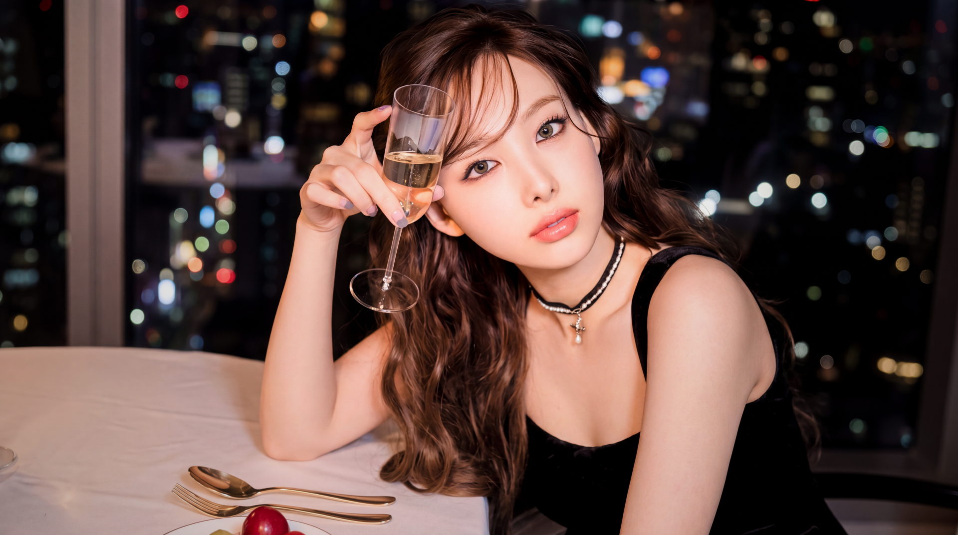 5K Ultra HD wallpaper of a glamorous young woman in K-pop style, holding a champagne flute at a candlelit table with blurred city lights behind her.