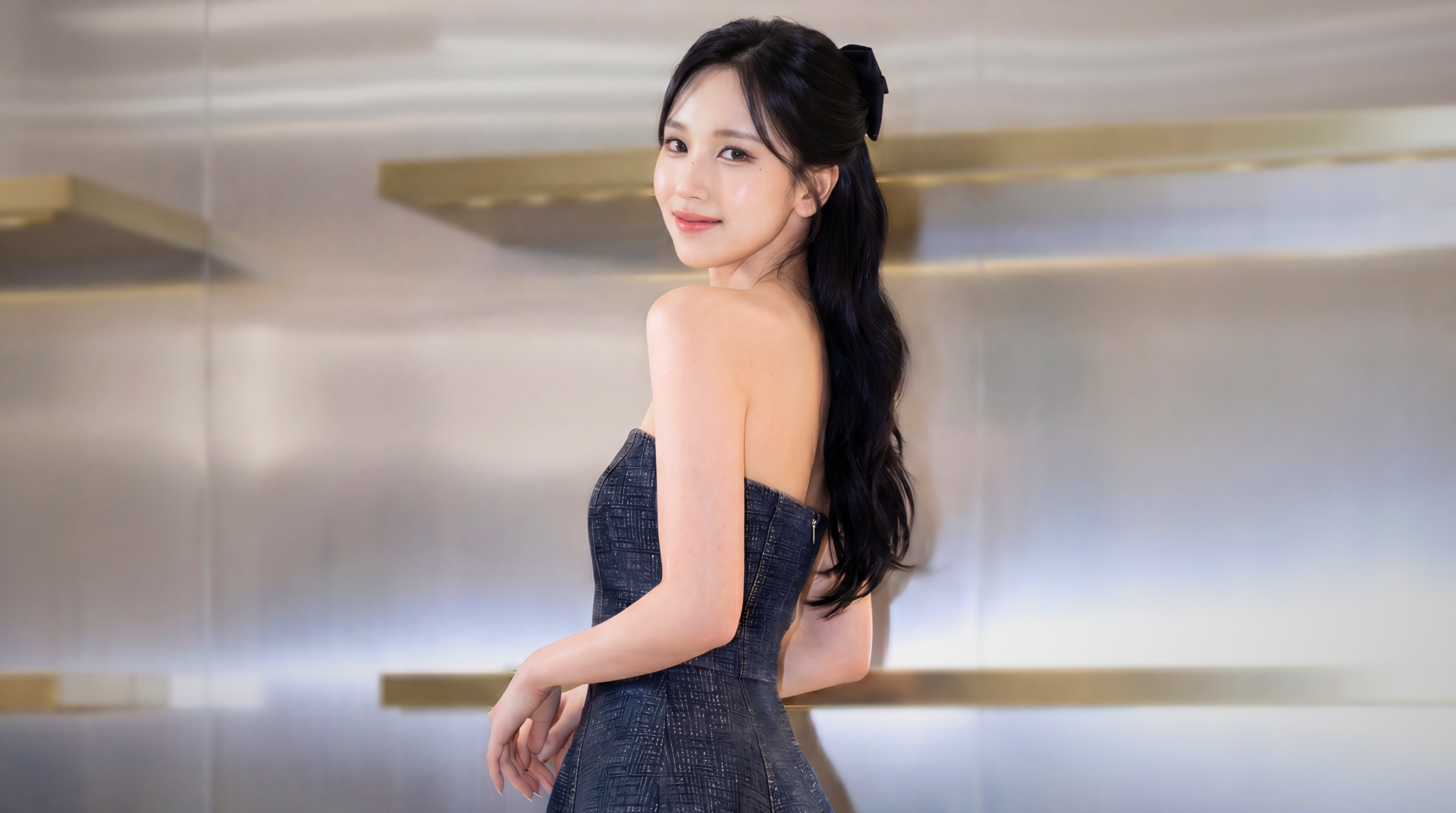 5K Ultra HD desktop wallpaper: a young woman in a strapless navy gown glances over her shoulder, long dark hair tied back, soft studio lighting and minimalist golden shelves behind her.