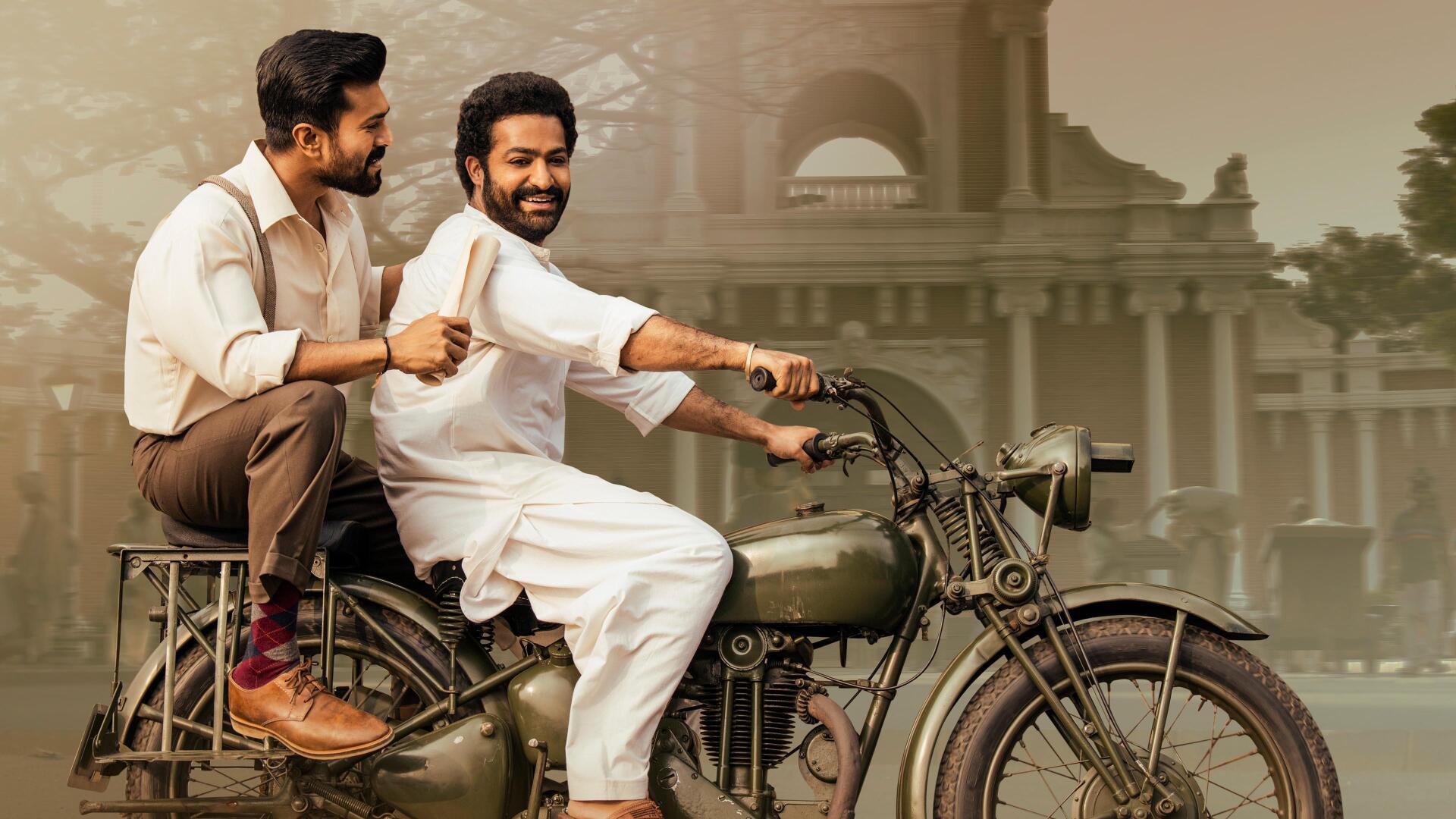 RRR 4K Ultra HD PC Desktop Wallpaper and Background: two smiling men on a vintage motorcycle riding past a stately colonial-style building.