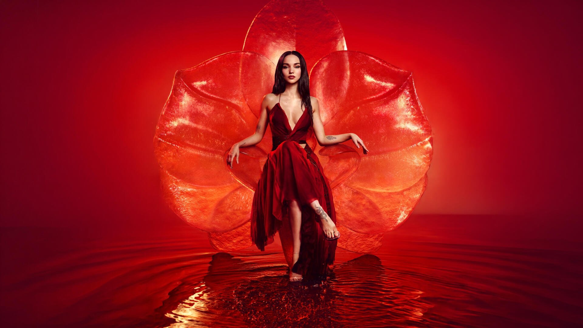 Woman in a flowing red gown stands in shallow reflective water before a stylized red petal backdrop — dramatic 5K Ultra HD PC desktop wallpaper.