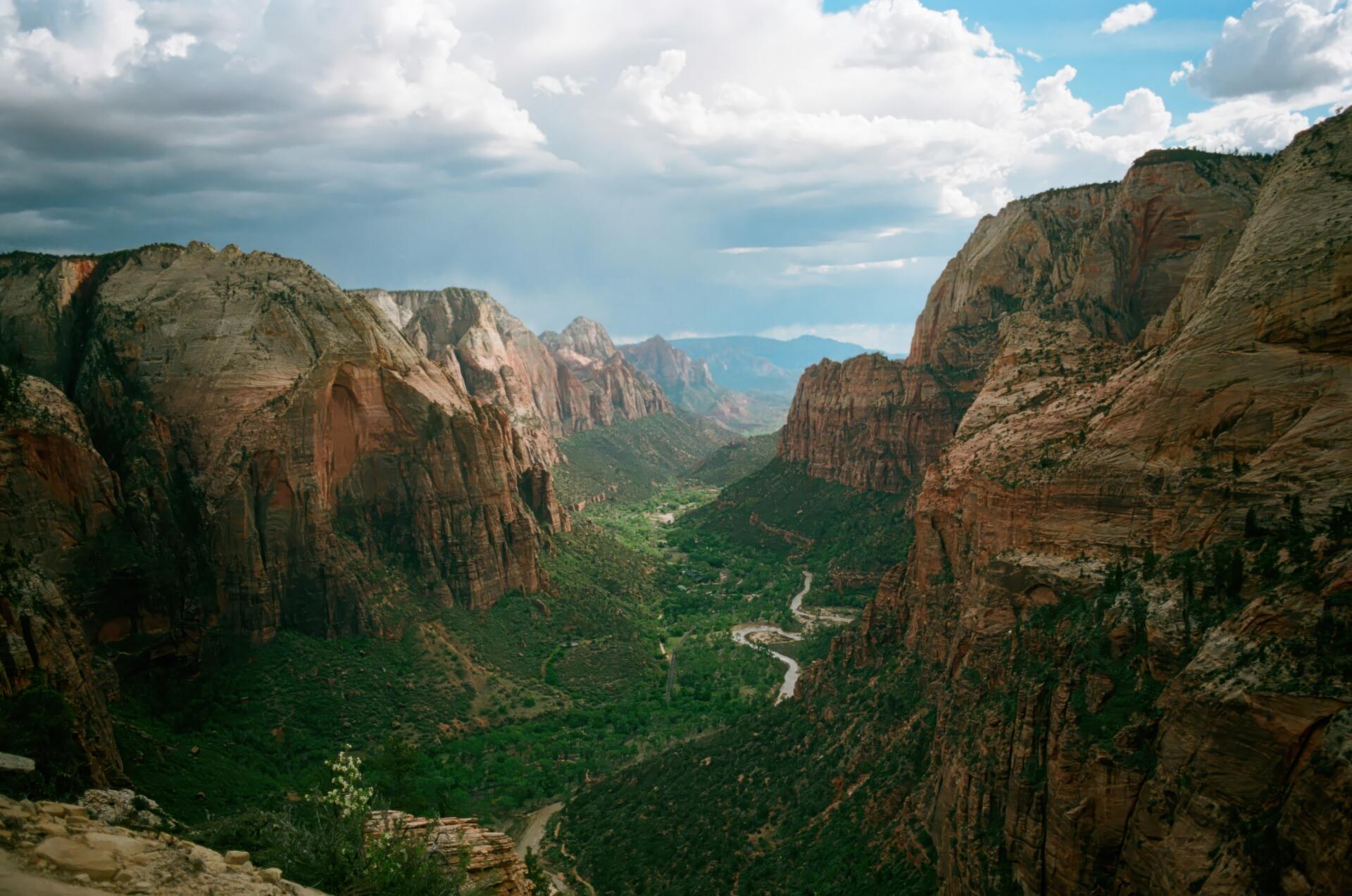 4K Ultra HD PC desktop wallpaper of Zion National Park canyon with towering red-rock mountains, a green valley with trees and a winding river under a partly cloudy sky.