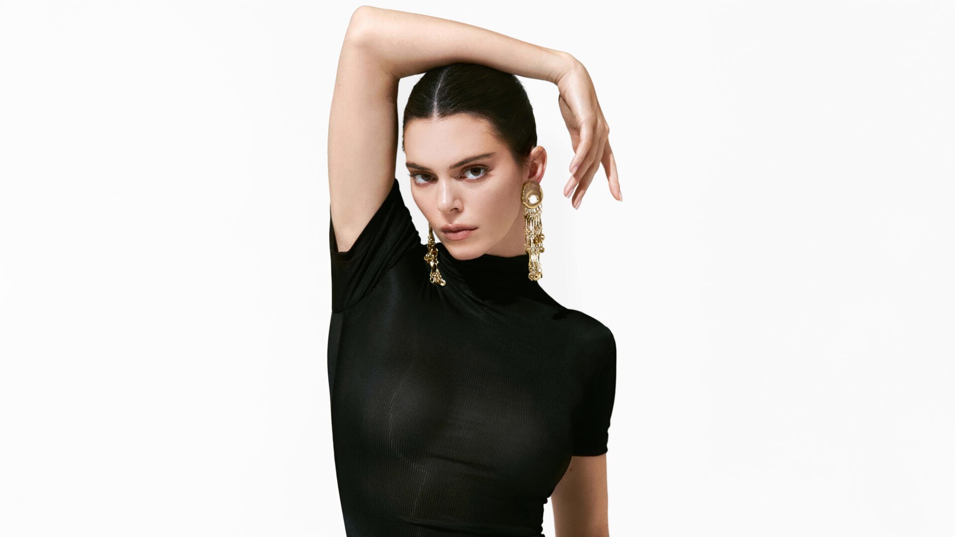 5K Ultra HD desktop wallpaper: fashion portrait of a poised model in a fitted black top, arm raised, wearing bold dangling earrings on a clean white background.