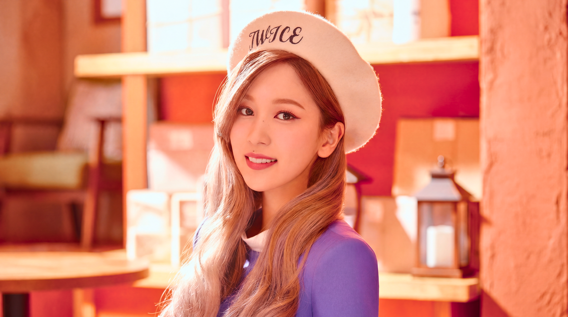 5K Ultra HD desktop wallpaper of a smiling young woman in a white beret embroidered TWICE, long hair and purple top, warm wooden shelves and lantern-style decor in the background.