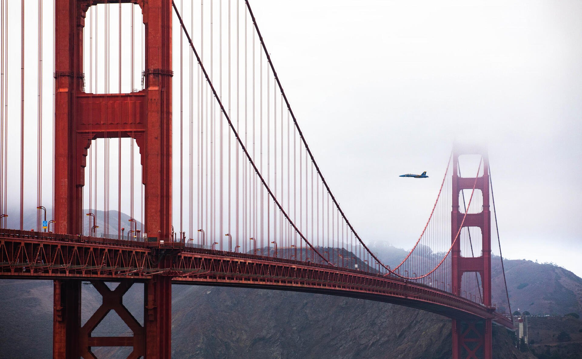 Blue Angels Boeing F/A-18E/F Super Hornet flies past the Golden Gate Bridge, a suspension bridge, in this 5K Ultra HD desktop wallpaper.