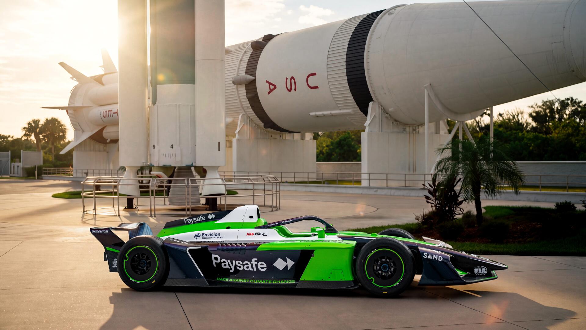 Envision Racing Formula E race car beneath a rocket at sunset, 8K Ultra HD PC desktop wallpaper and background.
