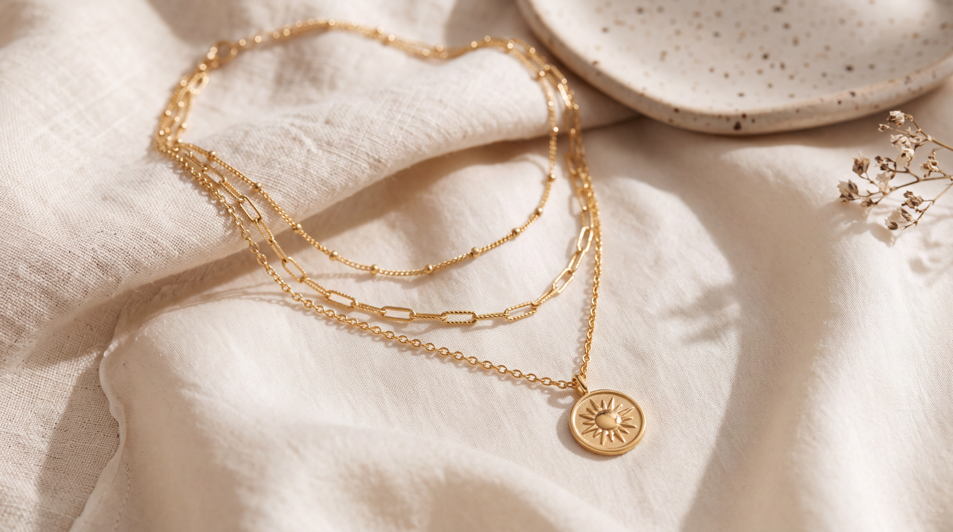 5K Ultra HD desktop wallpaper featuring layered gold necklaces and a sunburst pendant on a soft cream background.